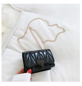 Detail of glossy black quilted bag featuring heart buckle and gold metal chain strap
