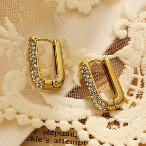 Close-up of gold U-shaped earrings with white zircon on lace and vintage book