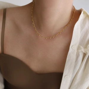 Close-up of a delicate gold beaded lace necklace layered on a white shirt