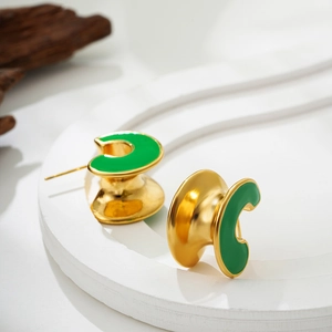 Detail view of C-shaped 18K gold earrings with green enamel on a white geometric stand