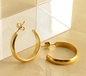 Close-up of polished gold-plated C-shaped hoop earrings with butterfly backs