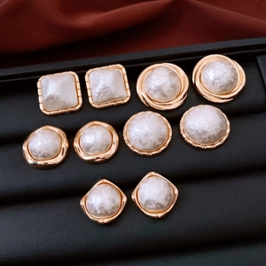 Macro view of assorted gold plated geometric stud earrings with pearl centers and textures