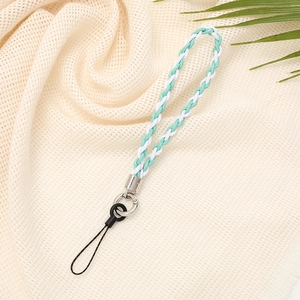 Close-up of green and white braided phone strap on beige fabric with palm leaf decor
