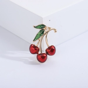 Detailed view of red enamel cherry brooch with green leaves and gold metal base