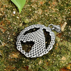 Close-up of silver hollow horse head pendant with textured mesh on natural moss ground