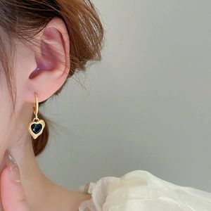 Close-up of heart-shaped black enamel drop earrings on a model in vintage gold finish