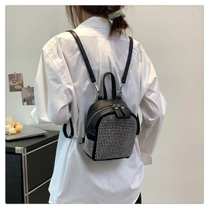 Detail of black mini backpack with silver rivets and adjustable straps on a model