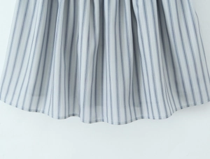 Detailed macro view of the striped dress hem featuring delicate pleats and soft blue fabric