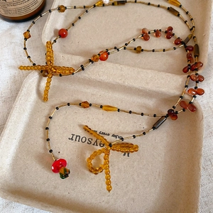 Detail view of crystal beaded necklace featuring amber bow, cross, and red mushroom charms
