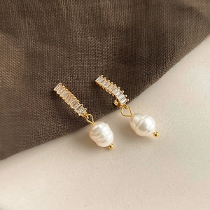 Detail of baroque pearl earrings with sparkling zircon stones on textured fabric