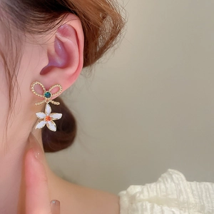 Close-up of model wearing gold-plated bow and white flower earrings with green gems