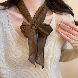 Detailed view of dark brown paisley silk scarf necklace on a chic beige knit sweater