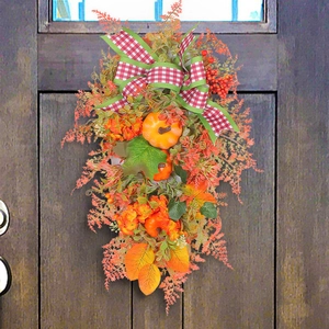 Autumn wreath with pumpkins, berries and plaid bow hanging on a dark wood door