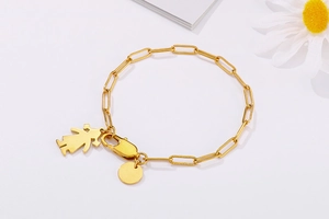 Détail du bracelet chaîne trombone dorée avec pendentif silhouette de fille et médaille