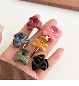 Close-up of six colorful matte mini bow hair claws held over a decorative book