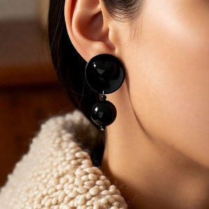 Close-up of black retro acrylic earrings with heart relief on a model wearing a beige knit sweater