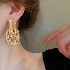Orecchini ovali geometrici placcati oro con texture ondulata indossati da modella