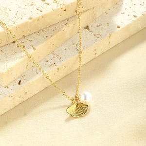 Gold ginkgo leaf necklace with a white round pearl pendant on a stone background