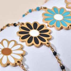 Close-up of a daisy pendant with black enamel finish and blue beaded chain details