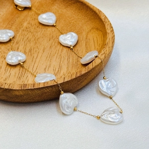 Detail of elegant gold chain necklace featuring heart-shaped pearls on a silk background