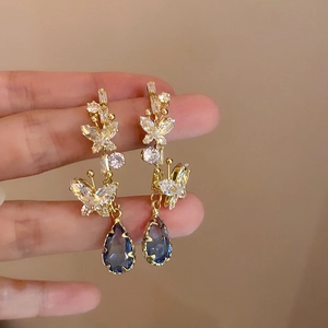 Detail of long drop butterfly earrings with gold finish and blue teardrop crystal