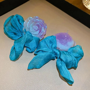 Close-up of elegant blue silk bow earrings with iridescent resin rose and silver pins