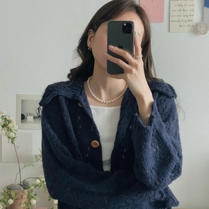 Detail of elegant white pearl necklace paired with a navy knit cardigan and wood buttons