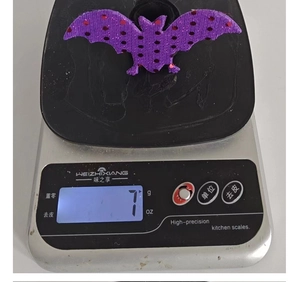 Detailed view of a purple glitter bat slap bracelet charm on a digital scale weighing 7 grams