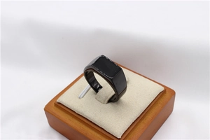 Macro view of a minimalist black square signet ring displayed on a beige velvet holder