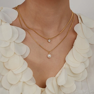 Detailed view of layered gold necklace featuring a zircon pendant and white pearl charm