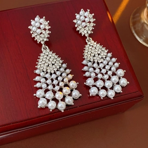 Detailed close-up of vintage pearl tassel earrings with rhinestones on red wood box