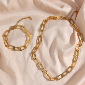 Golden paperclip chain necklace and bracelet set displayed on elegant champagne silk fabric