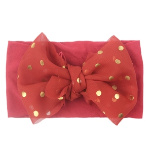Close-up of red nylon baby headband with a large gold polka dot lace bow detail