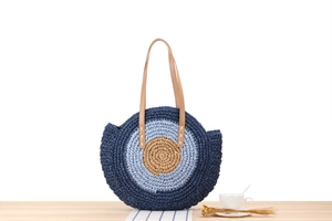 Detail of round straw beach bag showing tricolor woven design and brown leather straps