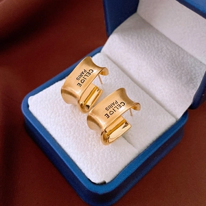 Macro detail of gold plated C-shaped earrings with brushed texture and engraved lettering