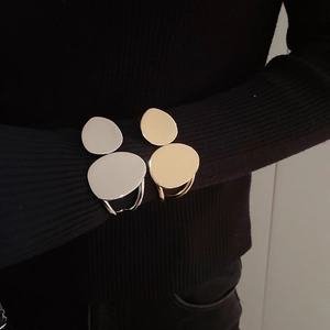Close-up of irregular oval layered gold and silver bracelets on black sleeve cuff
