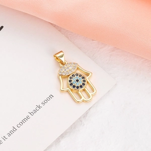 Macro shot of gold Hamsa hand pendant with blue and white crystals on white card