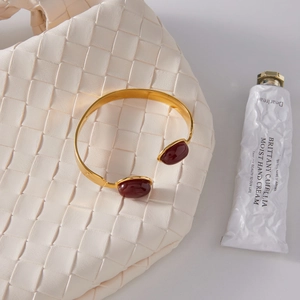 Detailed close-up of a gold C-shaped titanium steel bracelet with red agate gemstones