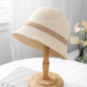 Stylish beige knitted bucket hat with brown stripes on a wooden stand by the window