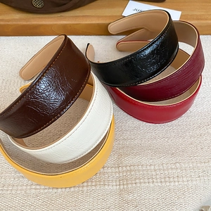 Detail of pleated PU leather headbands with contrasting yellow stitching and glossy texture