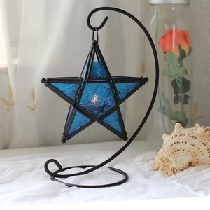 Close-up of a blue star-shaped embossed glass lantern on a black metal C-stand holder