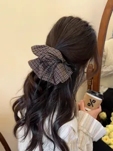 Brown plaid scrunchie with a black ribbon bow shown on a woman's low ponytail