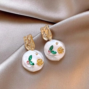 Macro shot of vintage floral earrings with freshwater pearls and green leaves on silk