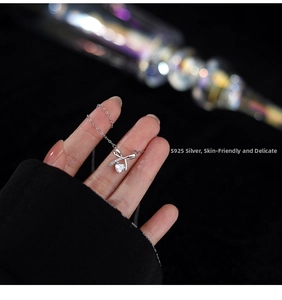 Close-up of S925 sterling silver bow necklace with heart crystal held by hand