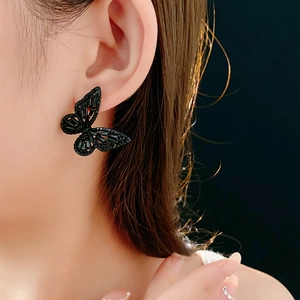 Close-up of a woman wearing black butterfly stud earrings with sparkling crystals