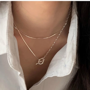 Dettaglio della collana d'argento a due strati con chiusura OT su una camicia bianca