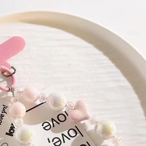 Pink and pearlescent heart beaded phone charm chain on a white textured plate
