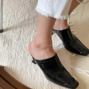 Detail of a minimalist 925 sterling silver chain anklet worn with black mule shoes
