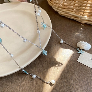 Elegant ocean-style necklace with silver chain, blue starfish, shells, and white pearls
