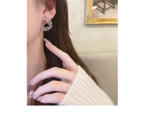 Close-up of elegant leaf-shaped zircon stud earrings worn by a model in soft lighting